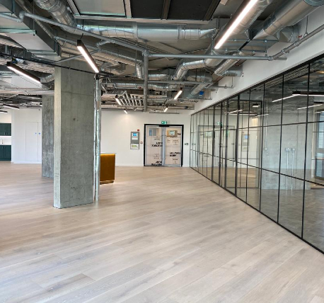 Commercial open plan office with timber floor, white walls, exposed ductwork ceiling and glazed partition wall to meeting area