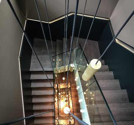 Penthouse stairwell with glazed balustrade, timber steps, black clad walls with handrail and long drop pendant lights
