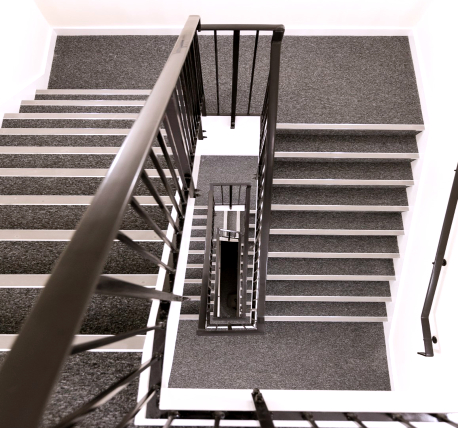 Office stairwell, looking down from the top floor, with grey carpet, stainless steel nosing and black balustrade