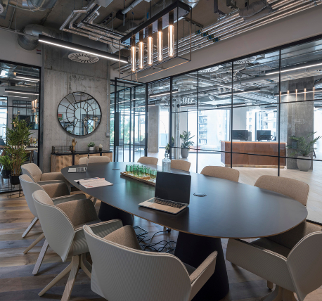 Meeting room with oval table and neutral chairs, timber flooring, glazed partitions and exposed ductwork ceiling.