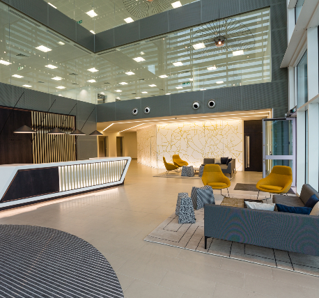 Commercial office reception area with bespoke white desk with cladding to the front, seating area and glazed partitions